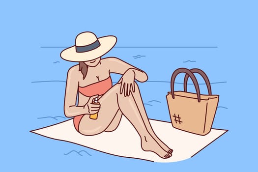 Woman applies sunscreen to protect herself from sun, relaxing on sea beach of tropical resort. Girl tourist uses sunscreen and counters ultraviolet rays, sitting on towel in hat and bikini