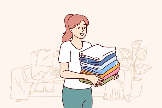 Kind woman housewife collects unwanted clothes around apartment to donate wardrobe items to charitable foundation. Housewife stands in room with scattered clothes and neatly stacks t-shirts in pile