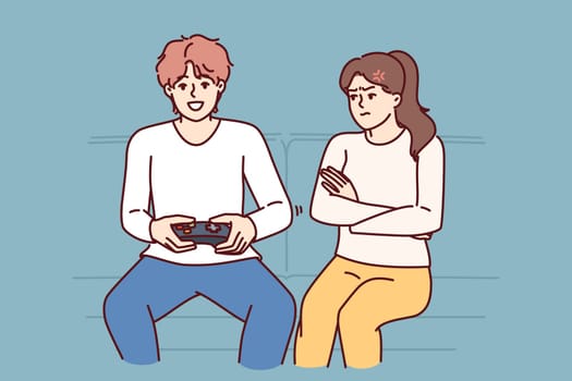 Woman is angry at husband who plays video game and does not want to do housework. Disgruntled girl sits on couch near boyfriend who is keen on video game, persuading him to go for walk