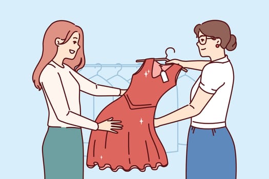 Woman picks up dry-cleaner dress standing in laundry room next to employee demonstrating cleaned clothes. Happy girl visitor to boutique, buys red evening dress for going to party.