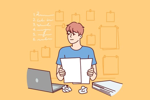 Man freelancer is doing paperwork, sitting at table with laptop and documents and thinking about plan for further actions. Guy does paperwork and makes list or checklist of future tasks