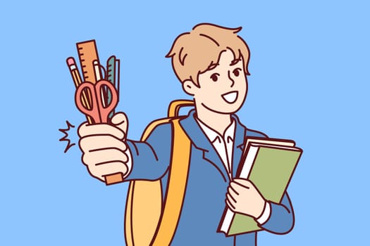 Little boy from elementary school with smile demonstrates stationery and books, standing with backpack. Concept of back to school, with child going to first grade and rejoicing at onset of september