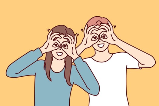 Funny man and woman make binoculars from fingers and look at screen smiling to cheer themselves up or friends. Funny guy and girl bring hands to eyes, demonstrating glasses gesture