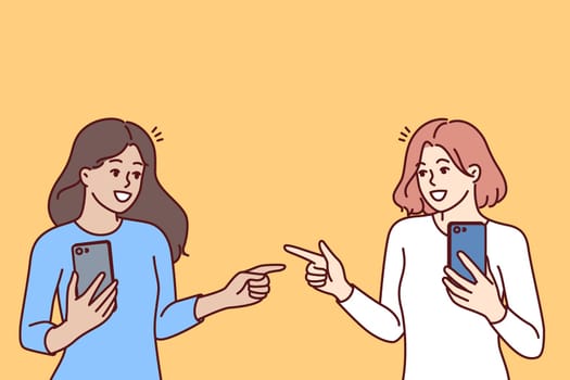 Women with mobile phones point fingers at each other, rejoicing at first meeting after acquaintance in social networks. Happy girls with phones, advertise applications for communication