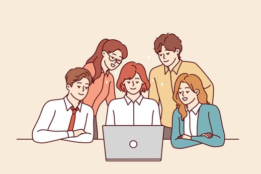 Successful business team looks at laptop screen together participating in corporate online meeting. Employees of consulting company in business clothes sit and stand near table with computer.
