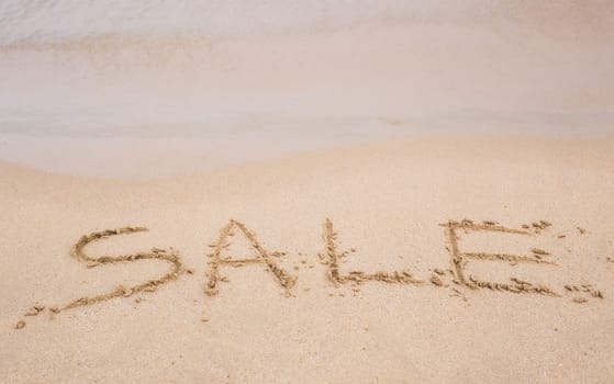 Summer sale handwritten in sand on a beach.