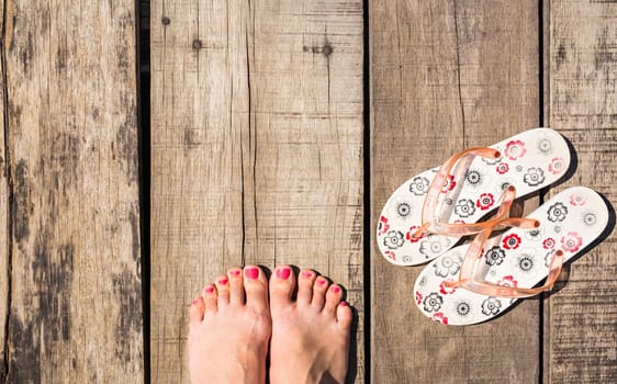 Female feet with flip-flops on wooden background, top view