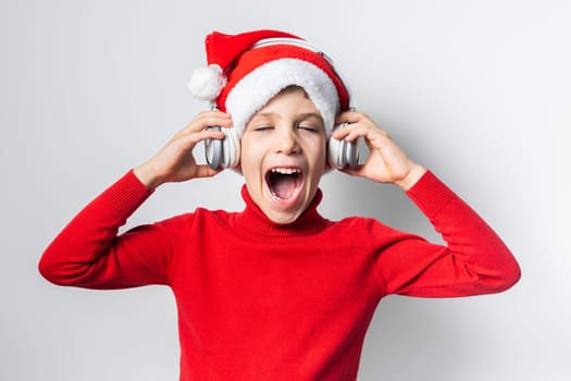 Child boy holds listening to Christmas music with funny Santa Claus hat on white