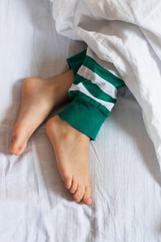 Child feet under the white blanket, top view.
