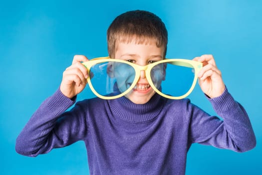 Cheerful little boy in big glasses express a surprised face isolated on blue background