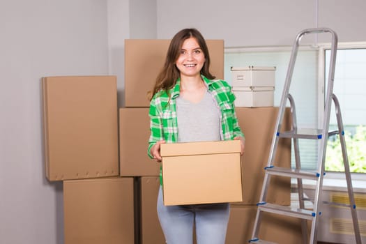 Portrait of woman carrying cardboard box in new house - Moving, new home and people concept.
