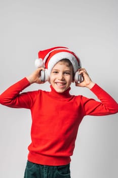 Child boy holds listening to Christmas music with funny Santa Claus hat on white