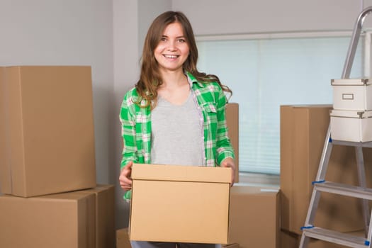 Portrait of woman carrying cardboard box in new house - Moving, new home and people concept.