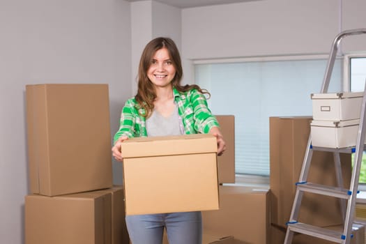 Portrait of woman carrying cardboard box in new house - Moving, new home and people concept.