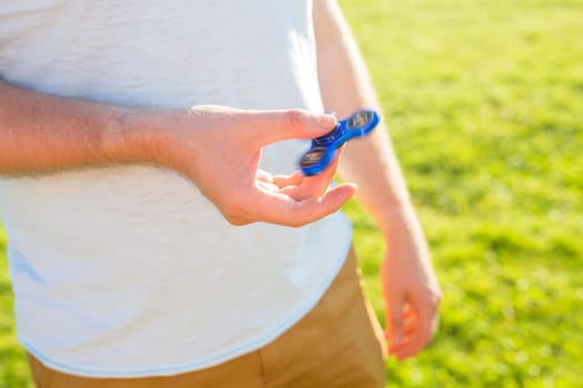 Close up of man playing with a blue hand spinner fidget toy.