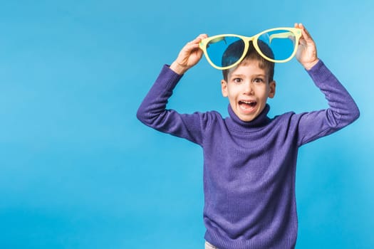 Cheerful little boy in big glasses express a surprised face isolated on blue background