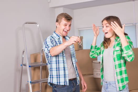 home, people, moving and real estate concept - Surprised woman looking at house keys in the hand of a man.