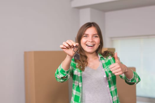 Happy apartment owner or renter showing keys and making thumbs up gesture.