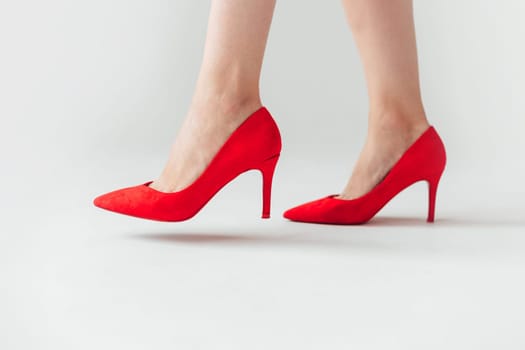 Woman in red high heels shoes is going, side view, leg in air before stand. White background.