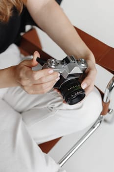Woman holds vintage film camera sitting chair on white background.