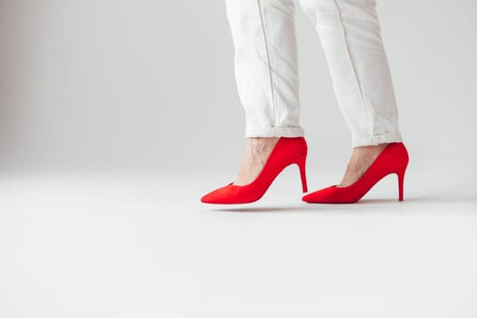 Woman in red high heels shoes and white pants is going, side view, leg in air before step. White background.