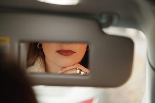Woman lips in vanity mirror while sitting in car