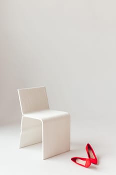 Female high heels shoes at white chair on white background. Minimalism.