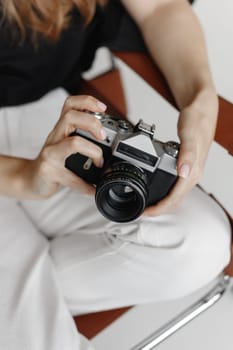 Woman holds vintage film camera sitting chair on white background.