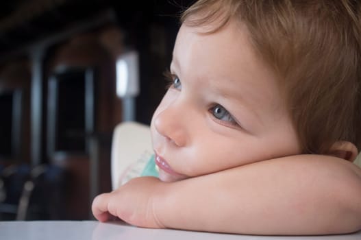 Pensive 2 years-old boy. He rests his head on his arm looking to the left