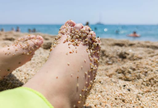 Childs feet covered in thick sand after bathing on the beach. Foot health for children