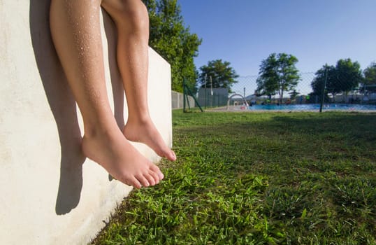 Barefoot boy sitting in the sun in a public swimming pool. Bone development in children concept