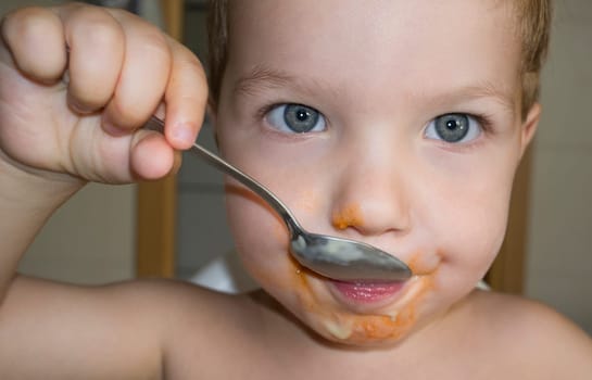 Baby boy eating by himself with spoon. Closeup