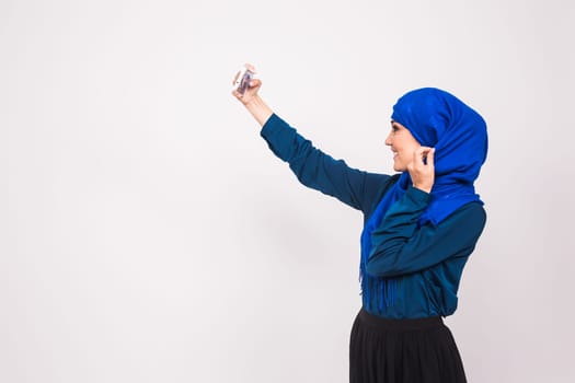 technology and people concept - muslim woman in hijab taking picture on smartphone over white background.