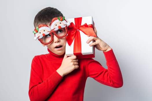 Happy boy in a red christmas holidays sweater and funny party glasses. Stylish boy with a Christmas gift have joyful on a white