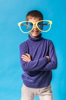 Cheerful little boy generation alpha in big glasses express a surprised face holds mockup board isolated on blue background with copy space.