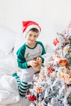 Child decorates Christmas tree. The boy is holding a Christmas toy. Morning before christmas at home. Generation alpha and gen alpha children
