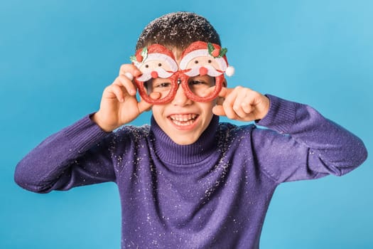 Portrait of attractive cheerful boy funny wearing festive santa eyeglasses eve christmas time isolated over bright blue color background.