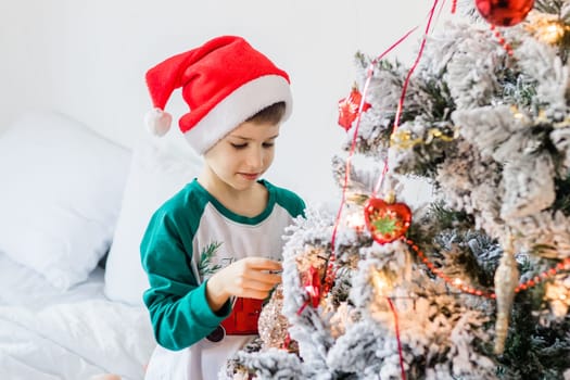 Child decorates Christmas tree. The boy is holding a Christmas toy. Morning before christmas at home. Generation alpha and gen alpha children