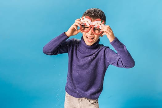 Portrait of attractive cheerful boy funny wearing festive santa eyeglasses eve christmas time isolated over bright blue color background.