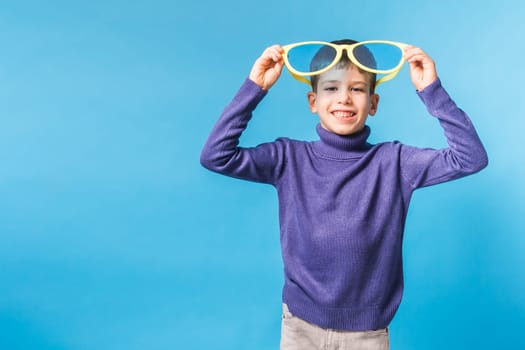 Cheerful little boy generation alpha in big glasses express a surprised face holds mockup board isolated on blue background with copy space.