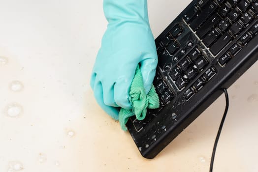 Cleaning computer keyboard in office with rubber protective glove, whiping with water and soap, cleaning dusty and dirty electronic, housework