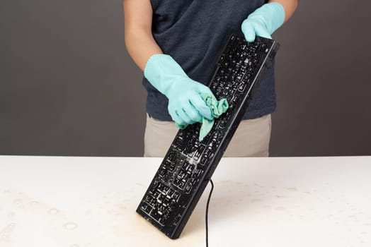 Cleaning computer keyboard in office with rubber protective glove, whiping with water and soap, cleaning dusty and dirty electronic, housework