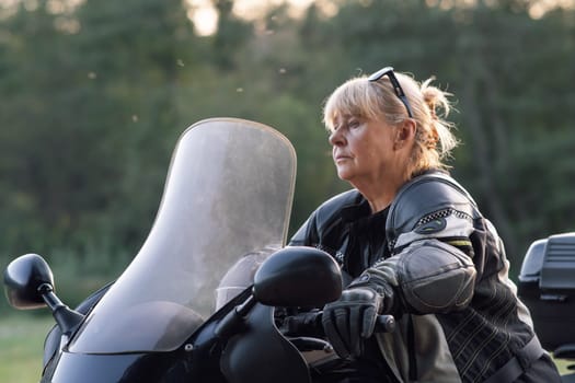 Blonde motorcycle tourist, wearing black gloves, sitting on her bike, begins to move carefully. Hobby motorcycle tourism. Healthy lifestyle. Excellent physical shape. Tourism and travel.
