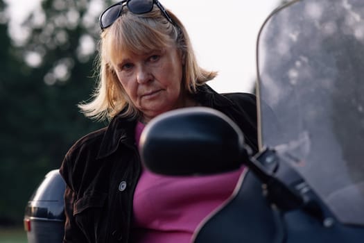 Hobby Motorcycle tourism. Seriously looking at camera adult blonde female motorcycle tourist, sitting on her bike. Healthy lifestyle. Excellent physical shape. Motorcycle equipment. Tourism travel.