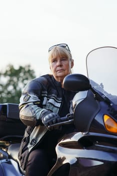 Beautiful vertical portrait of pretty middle-aged female motorcyclist sitting on her motorcycle on autumn day. Hobby motorcycle tourism. Healthy lifestyle. Excellent physical shape. Tourism travel.