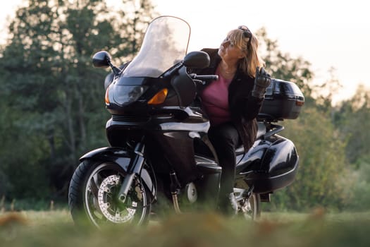 Motorcycle tourism. Pretty mature blonde in leather gloves at wheel of her bike is resting on autumn day. Hobby motorcycle tourism. Healthy lifestyle. Emotional relief. Tourism and travel.