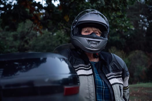 Motorcycle tourism. Unrecognizable woman in black closed motorcycle helmet next to her motorcycle. Hobby tourism. Healthy lifestyle. Excellent physical shape. Tourism and travel.