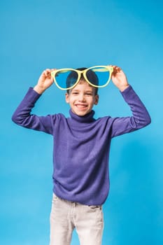 Cheerful little boy generation alpha in big glasses express a surprised face holds mockup board isolated on blue background with copy space.