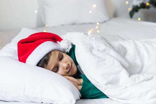 Sweet child boy sleeping in bed wearing Santa Claus hat in Christmas eve.