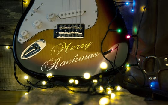 Old used vintage guitar with the inscription Merry Rockmas and Christmas lights on a wooden plank